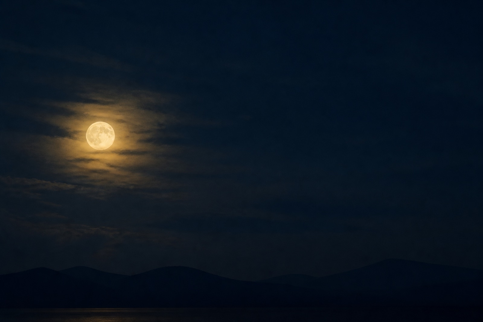 Vollmond über einer nächtlichen, stillen Landschaft in tiefem Blau